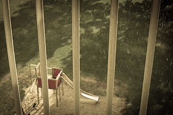 Rainy playground slide seen through vertical bars at night