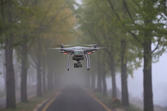 White drone hovering over a foggy tree-lined road