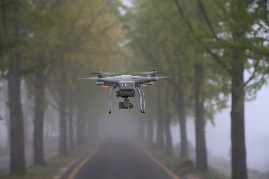 White drone hovering over a foggy tree-lined road