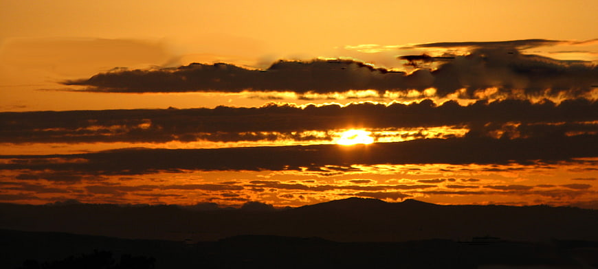 Dramatic golden sunset with layered clouds over dark hills
