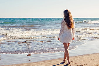 Woman in White Lace Dress Walking on Sandy Beach
