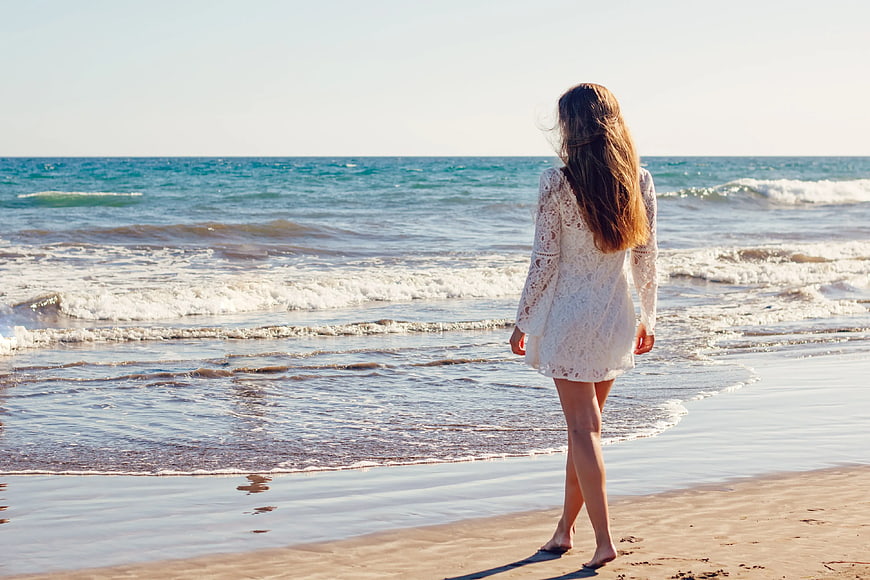 Woman in White Lace Dress Walking on Sandy Beach