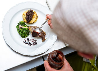 Chef plating gourmet duck leg with sauce and greens