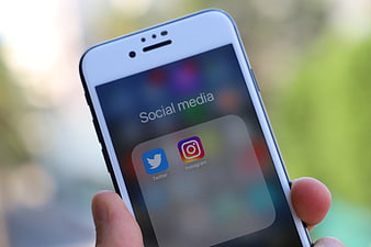 Hand holding smartphone displaying social media apps folder