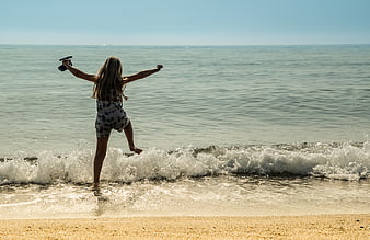 Girl jumping in waves at the beach with arms raised
