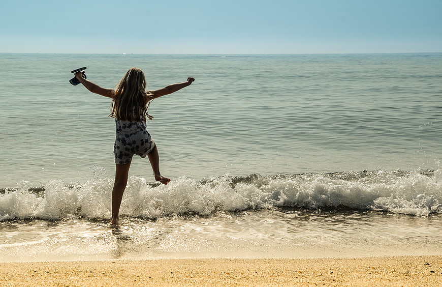 Girl jumping in waves at the beach with arms raised