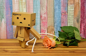Danbo cardboard robot kneeling with orange rose on wooden table