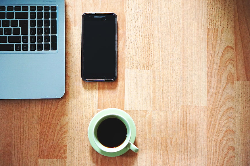 Flat lay of laptop, smartphone, and coffee on wooden desk