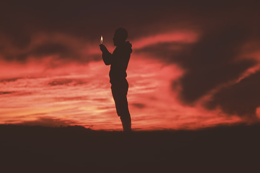 Silhouette of Man Holding Candle Against Red Sunset Sky