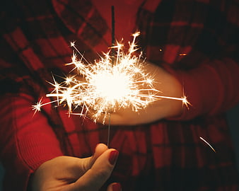 Person holding sparkler in red plaid shirt at night