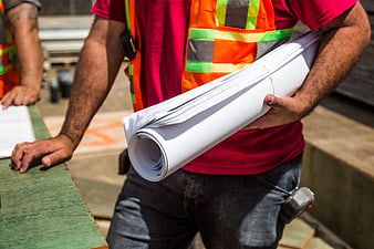 Construction Worker Holding Rolled Blueprints at Site