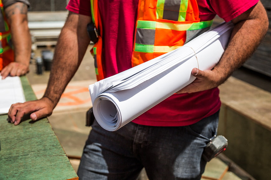 Construction Worker Holding Rolled Blueprints at Site