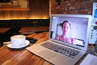 Woman video calling on laptop in cozy cafe with coffee