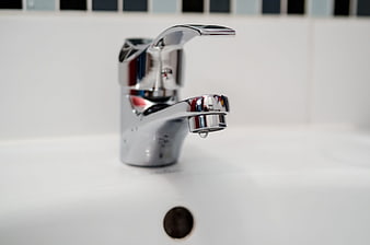 Chrome bathroom faucet with water droplet on white sink
