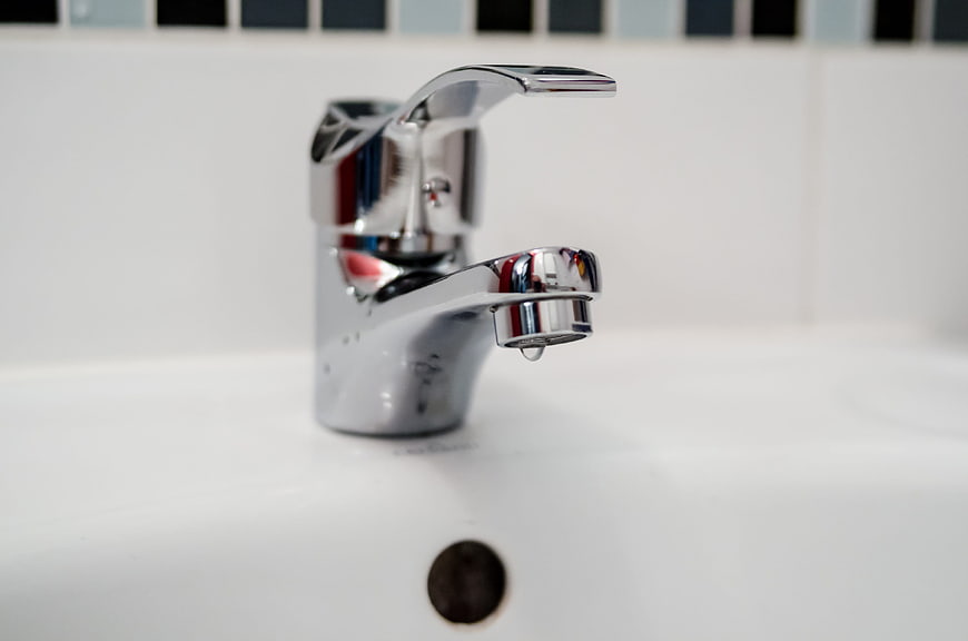 Chrome bathroom faucet with water droplet on white sink