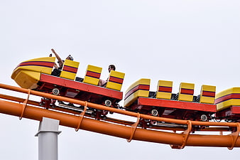 People riding a yellow and red roller coaster against a white sky