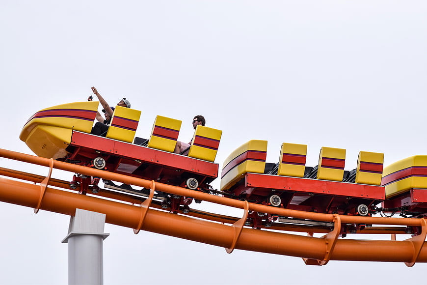 People riding a yellow and red roller coaster against a white sky