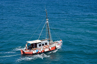 Red fishing boat sailing on blue sea with man on deck