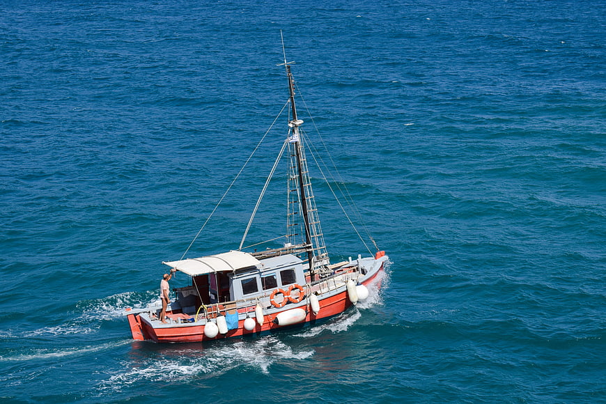 Red fishing boat sailing on blue sea with man on deck