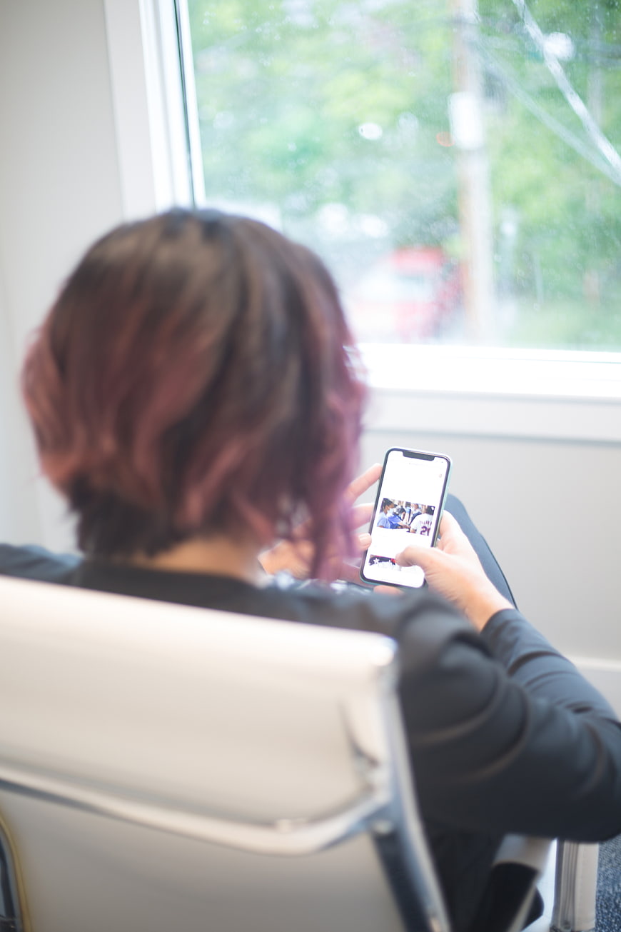 Woman with pink hair browsing smartphone by window