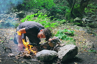 Man Tending Campfire in Lush Green Forest
