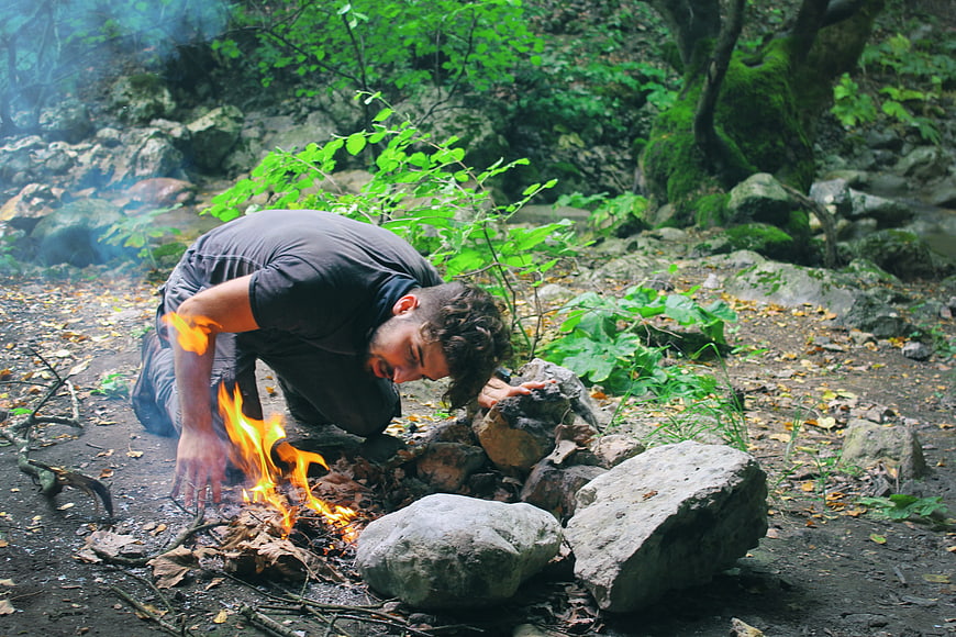 Man Tending Campfire in Lush Green Forest