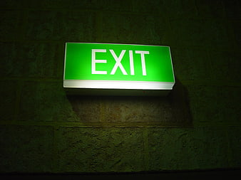 Glowing green exit sign mounted on dark textured brick wall