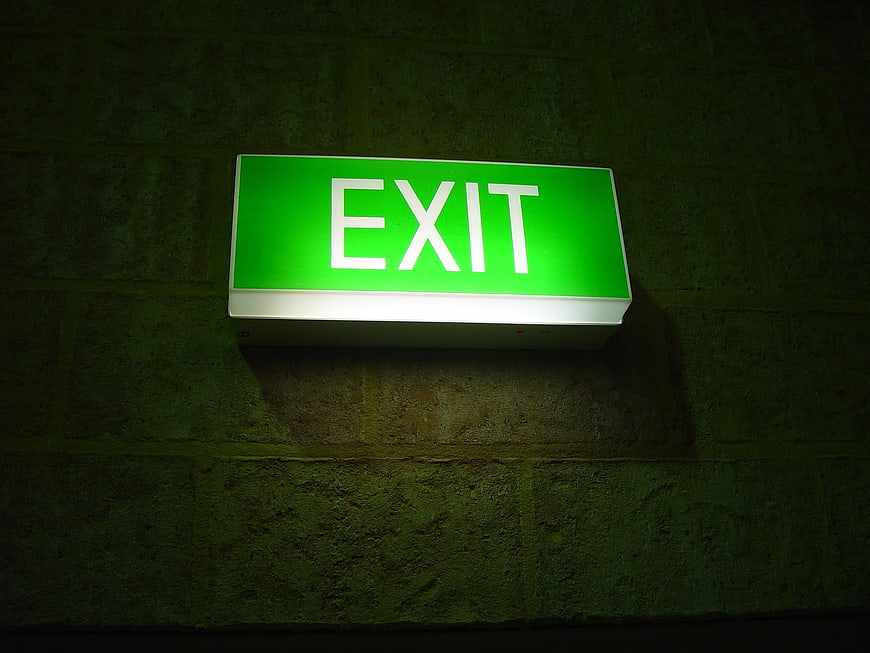 Glowing green exit sign mounted on dark textured brick wall