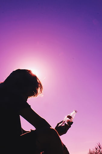 Silhouette of Man Holding Glass Bottle Against Purple Sunset Sky