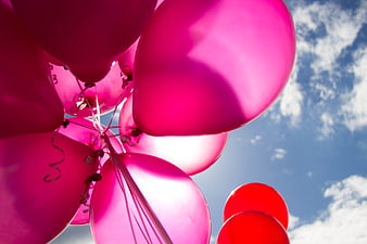 Pink and red balloons against a blue sky with clouds
