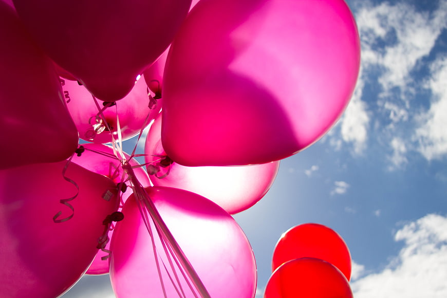 Pink and red balloons against a blue sky with clouds