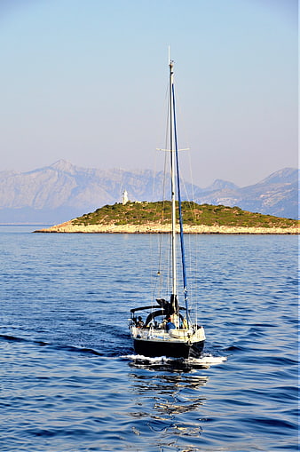 Sailboat Cruising Past Mediterranean Island with Lighthouse