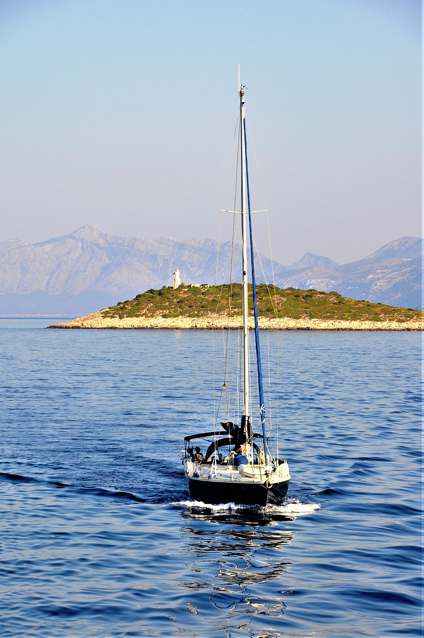 Sailboat Cruising Past Mediterranean Island with Lighthouse