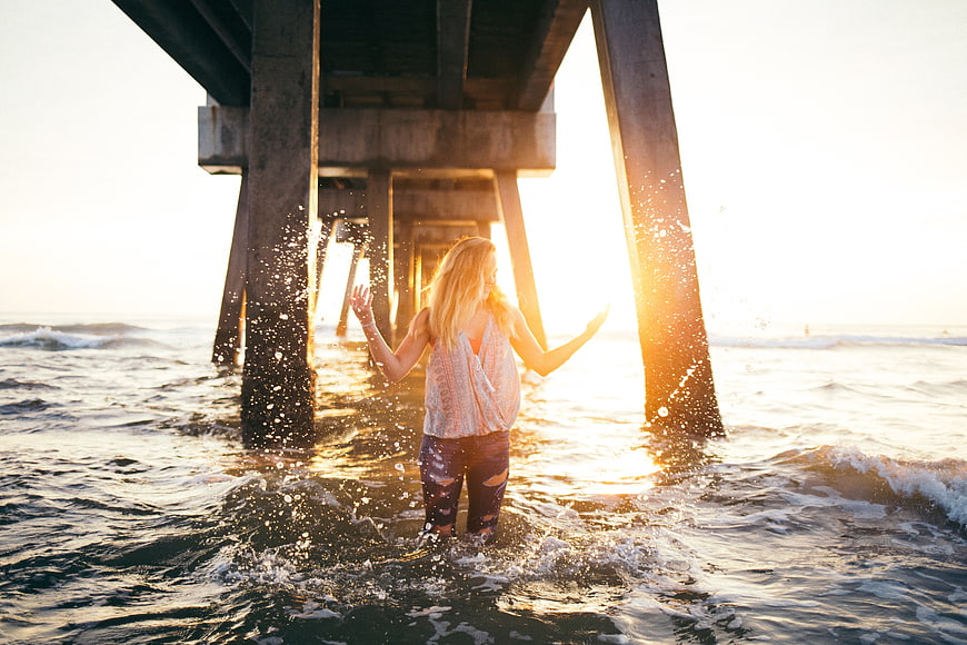 Woman splashing water under pier at golden hour sunset