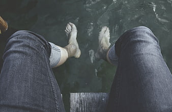 First-person view of bare feet dangling over water from a dock