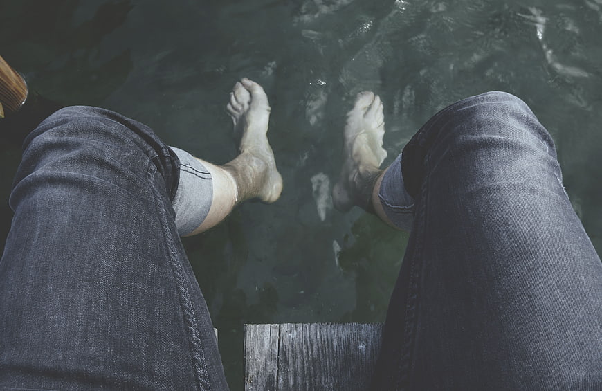 First-person view of bare feet dangling over water from a dock