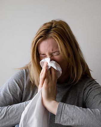 Woman sneezing into tissue with closed eyes