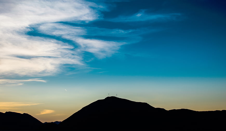 Silhouette of Mountain with Wind Turbines Against Blue Sky