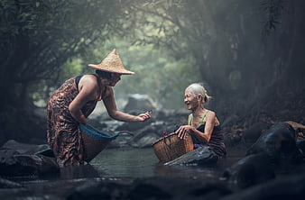 Two women washing clothes in a misty Southeast Asian river