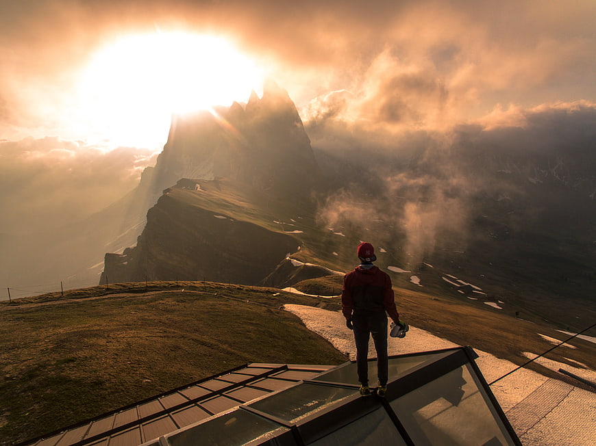 Hiker on Glass Platform Overlooking Dramatic Mountain Sunset