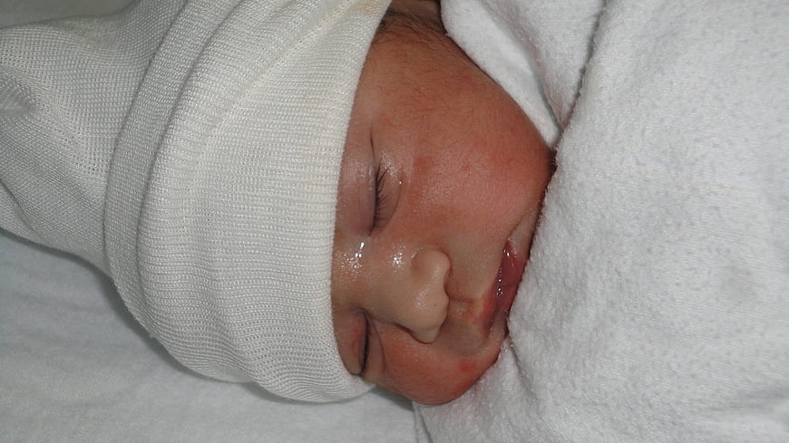 Newborn Baby Sleeping Peacefully Wrapped In White Hospital Blanket