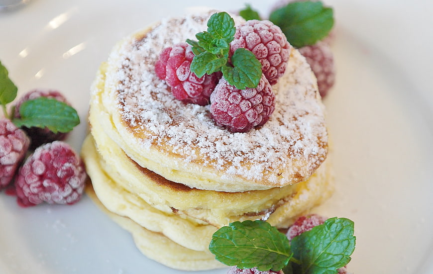 Stack of fluffy pancakes with raspberries and powdered sugar
