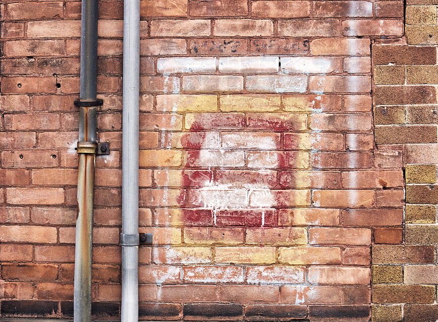 Textured Brick Wall with Pipes and Faded Graffiti