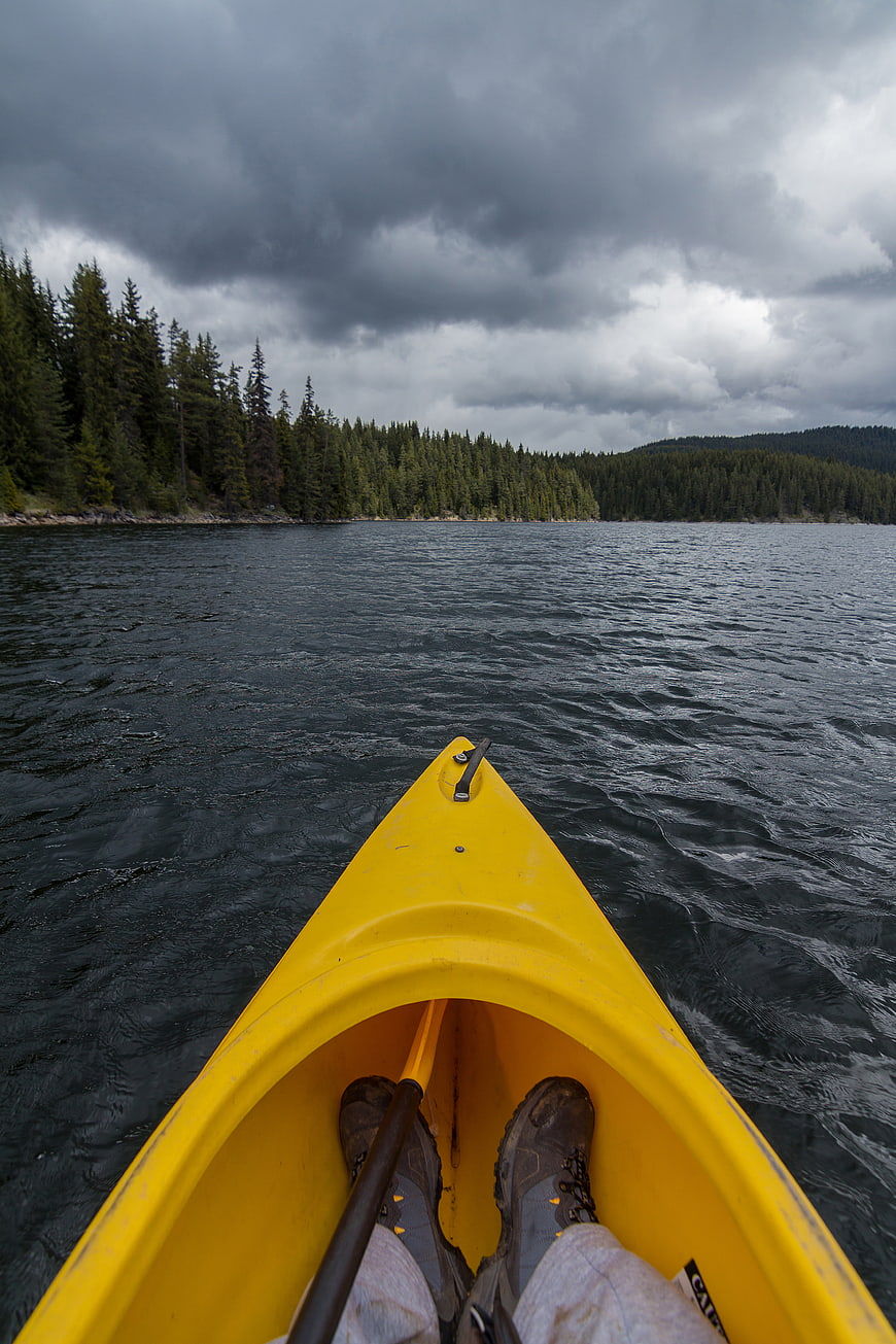 First-person view from yellow kayak on lake with forest