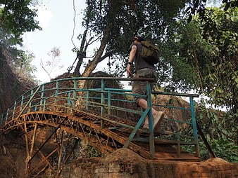 Hiker with backpack crossing rustic metal bridge in jungle