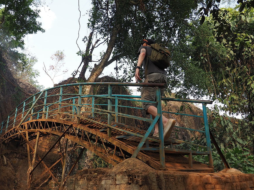 Hiker with backpack crossing rustic metal bridge in jungle