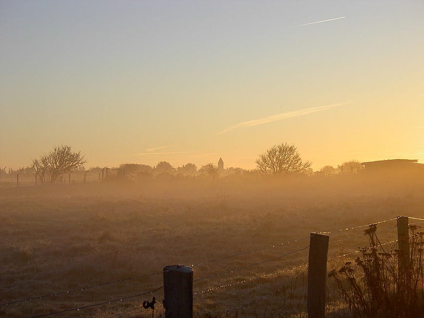 Frosty rural landscape with fog and sunrise behind fence