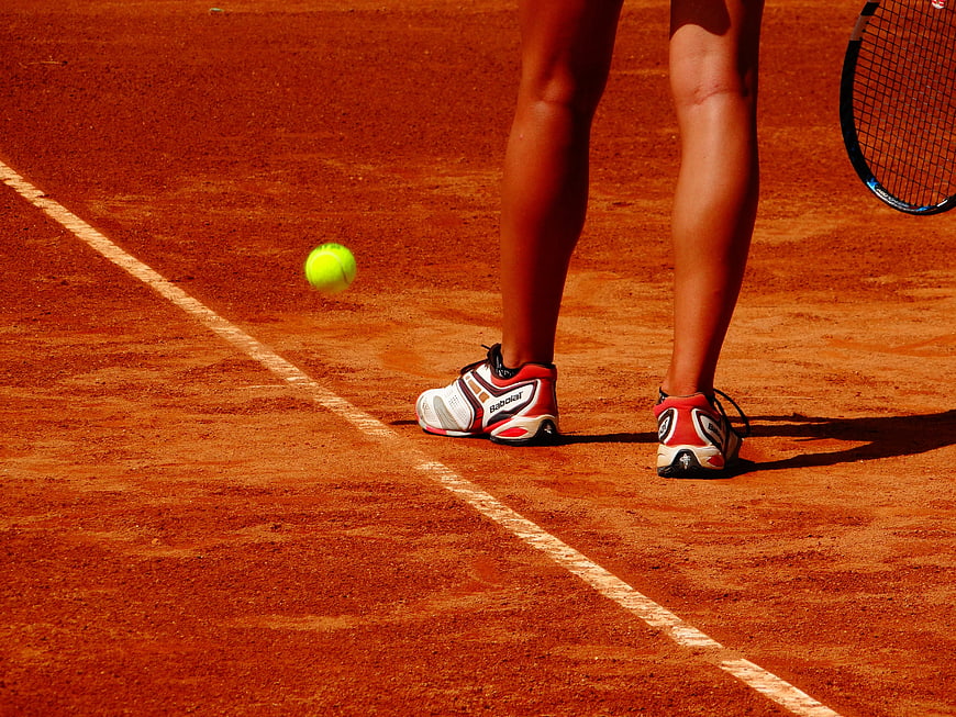 Tennis Player Legs On Red Clay Court With Ball And Racket