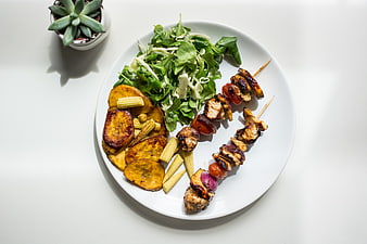 Top view of grilled chicken skewers with plantains and salad