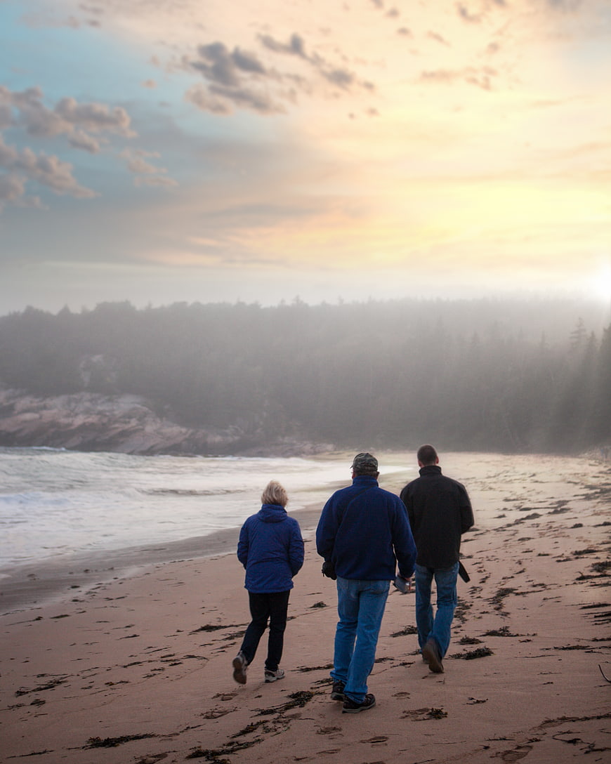 Three People Walking on Sandy Beach at Sunset